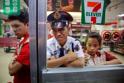 Varias personas observan desde el interior de una tienda mientras un policía investiga cerca del cuerpo de un hombre asesinado por un pistolero desconocido en Manila (Filipinas), el 18 de octubre de 2016. Un cartón en el que se podía leer "Pusher Ako, Wag Tularan", que se traduce como "Soy un vendedor (de drogas), no seas como yo", fue encontrado cerca del cuerpo.