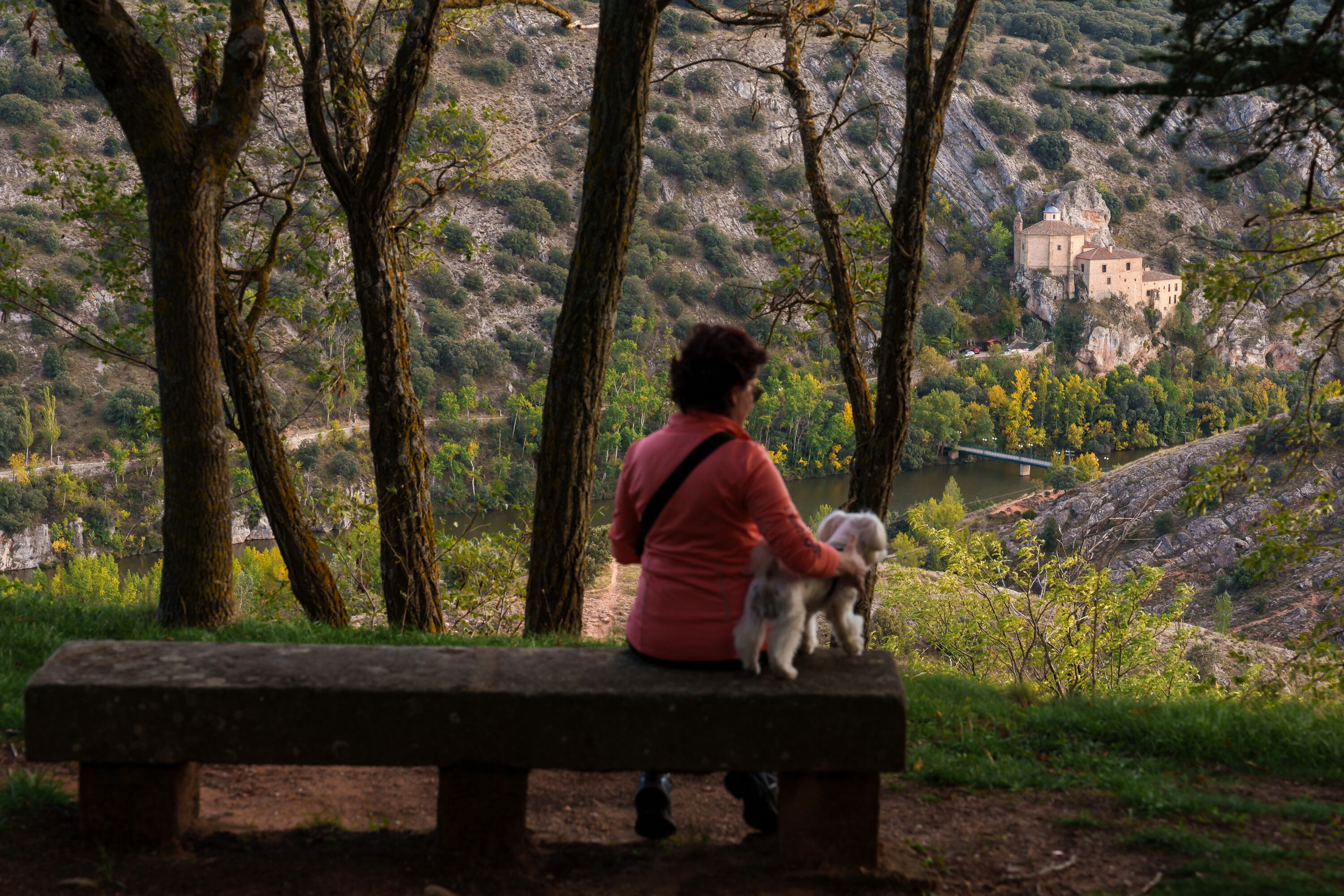 Una paseante descansa en un banco con vistas al Duero y a la ermita de San Saturio, en el entorno del parador de Soria.