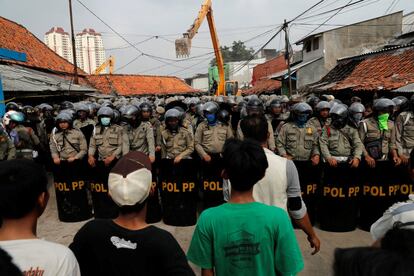 Un cordón policial separa a los residentes de Luar Batang que ven como se llevan a cabo las labores de demolición de sus casas, en Yakarta, Indonesia.