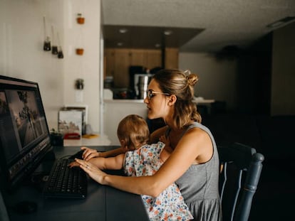 Una madre intenta trabajar con su hija encima.