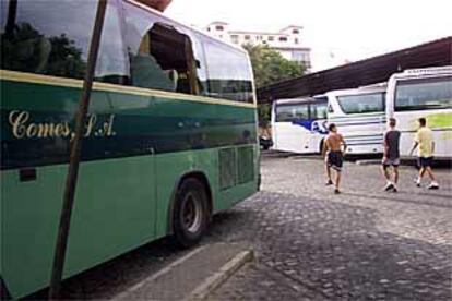 Tres jóvenes viajeros pasan junto a un autobús con la luna rota por los piquetes, que obligaron al conductor a volver ayer a Sevilla.