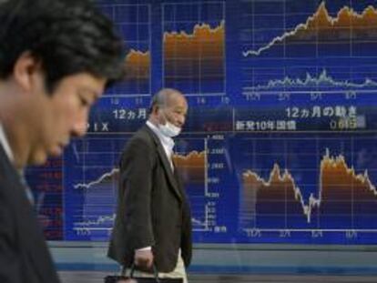 Dos hombres caminan junto a una pantalla informativa que muestra información bursátil en Tokio (Japón). EFE/Archivo
