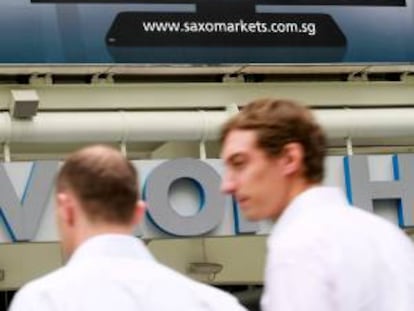 Dos hombres caminan junto a una pantalla que muestra la información de la bolsa en Singapur. EFE/Archivo
