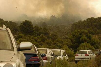 Vehículos estacionados en una de las carreteras cortadas por el incendio del bosque de La Torre de les Maçanes.