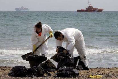 Operarios de limpieza retiran los restos de fuel de la arena.