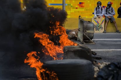 Dos jóvenes esperan sentados frente a una barrica durante las protestas contra el presidente Nicolás Maduro en Caracas (Venezuela).