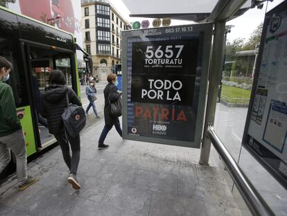 Un cartel contra la tortura colocado en una marquesina de San Sebastián tapa el que promociona la serie 'Patria'.