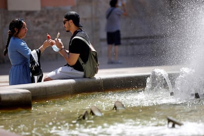 Dos personas se toman un helado junto a una fuente en Valencia.