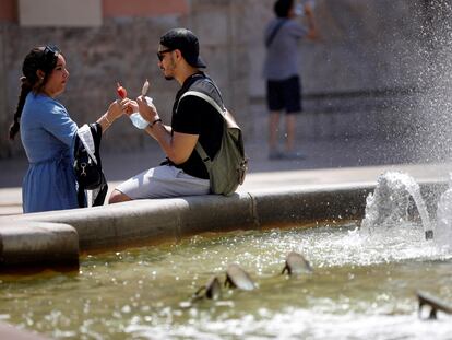 Dos personas se toman un helado junto a una fuente en Valencia.