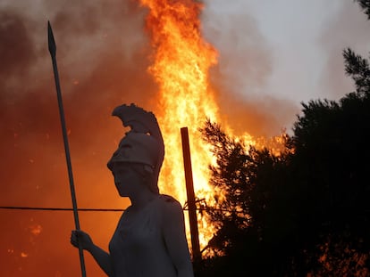 Uma estátua da deusa grega Atena, iluminada por um incêndio ao fundo, em Varympompi, norte de Atenas, na Grécia, em 3 de agosto.