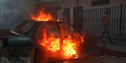 Um manifestante passa junto a um carro em lumes utilizado como barricada.