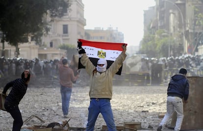 Un manifestante exhibe una bandera egipcia mientras otros tiran piedras a un cordón policial al lado del Ministerio del Interior, en El Cairo, este viernes.