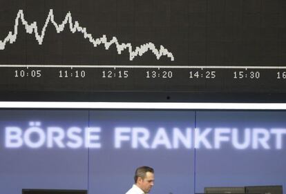 Un bróker camina frente a una pantalla que refleja el índice DAX alemán.