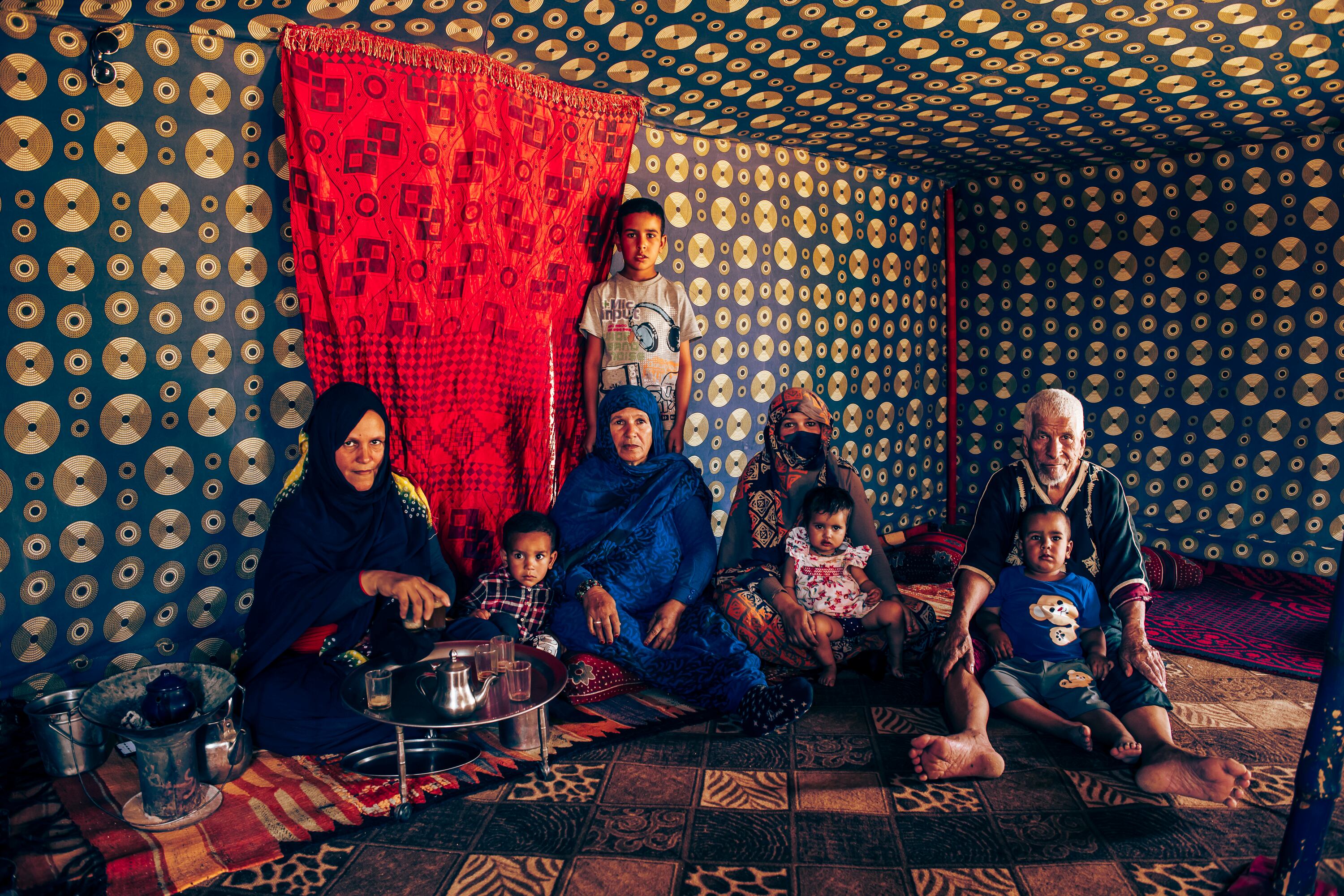 La familia de Salek Mohamed Salem, de 82 años (a la derecha), y Ala Rabub Handy, de 70 (en el centro, de azul), se reúne bajo la jaima de los abuelos en Auserd (Tinduf). Sus hijas y nietas están preocupadas por su estado de salud, el calor es insoportable y no tienen aire acondicionado, explican. Ambos nacieron españoles en el Sáhara Occidential, cuando era la provincia número 53. Huyeron en 1975, cuando Marruecos se anexionó la excolonia española. Desde entonces dependen por completo de la ayuda internacional para sobrevivir, pero cada vez están más apurados. 