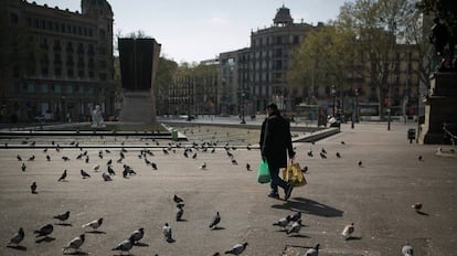 Una persona camina cargado con la compra por plaza Catalunya donde solo quedan las palomas.