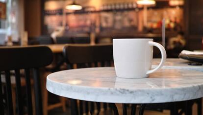 Una solitaria taza de café en una mesa de una cafetería.