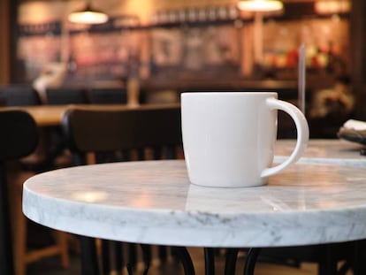 Una solitaria taza de café en una mesa de una cafetería.