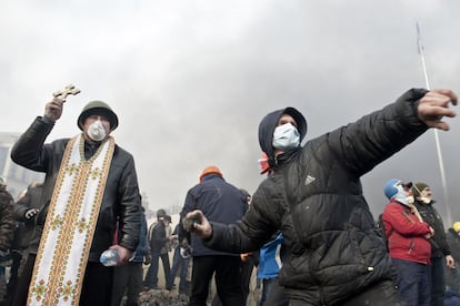 Um manifestante lança uma pedra contra a polícia, enquanto outro levanta uma cruz durante os confrontos na praça da Independência de Kiev.