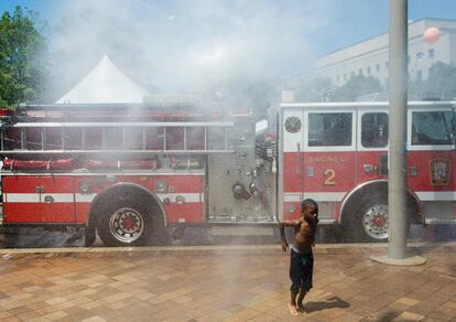 Un muchacho se enfría con una manguera de agua de un camión de bomberos en Washington, Estados Unidos.