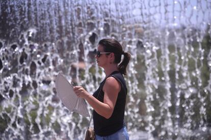 Una joven se abanica mientras pasa junto a una fuente del centro de Córdoba.