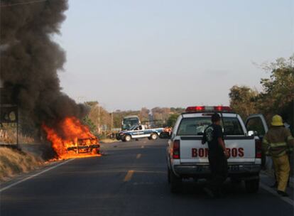 Bomberos tratan de controlar el fuego de la camioneta en la que cuatro policías han sido asesinados por varios sicarios.