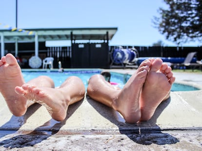 Dos adolescentes se apoyan en el bordillo de la piscina.