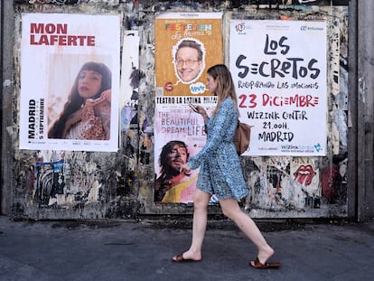 Una mujer pasa con su teléfono móvil por varios carteles de conciertos en una calle de Madrid.