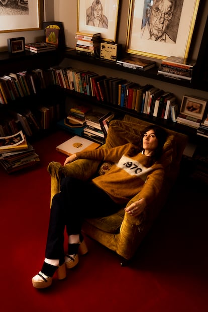 Bella Freud posa en la biblioteca de su casa. Lleva un jersey de su marca. 