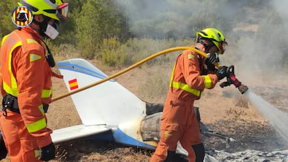 Dos bomberos apagan el fuego producido al estrellarse una avioneta en Requena (Valencia) este sábado.