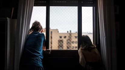 Dos niñas miran por la ventana en su casa durante el confinamiento por la pandemia del coronavirus, en abril de 2020.