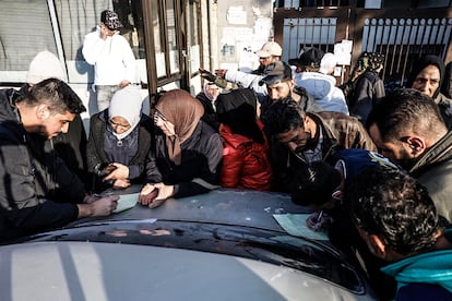 Un grupo de personas se amontona para ver si sus familiares aparecen en las listas de pacientes del hospital Muytahed de Damasco.