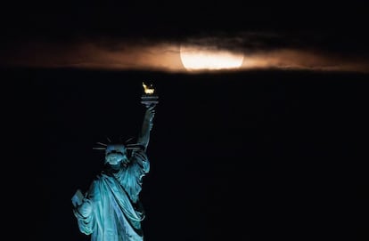 La luna rosada se eleva detrás de la estatua de la Libertad en la ciudad de Nueva York (EE UU).