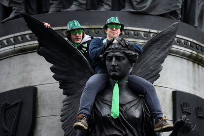 Dos hombre se sienta en una estatua para ver el desfile del Día de San Patricio en Dublín (Irlanda).