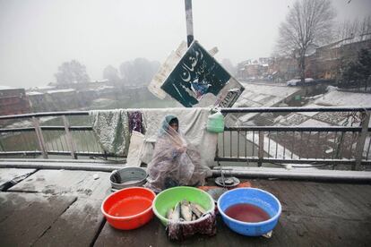 Una vendedora de pescado espera clientes envuelta en un plástico para protegerse del frío en Srinagar (India).