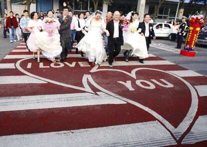 Un grupo de parejas recién casadas cruzan por un paso de peatones decorado con motivo de San Valentín, en Chengdu (China).