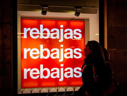 Viandantes ante un cartel de rebajas en una tienda.