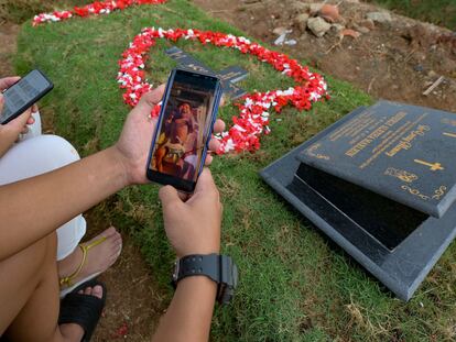 Tirsa Manitik y Erik Alexander muestran la foto de su bebé en un móvil cuando visitan la tumba de su hijo, que dio positivo por covid.19 antes de morir, en el Cementerio de Tegal Alur en Yakarta.