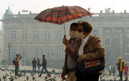 Una pareja camina con mascarillas frente al edificio del Congreso de Colombia debido a una enorme nube de humo que cubre el centro de la ciudad.