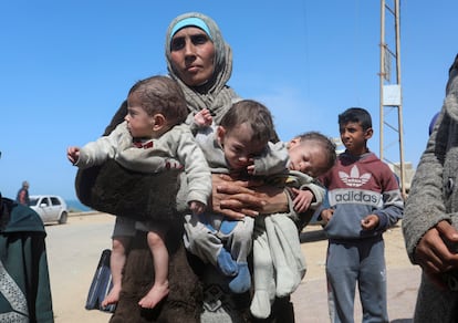 A Palestinian woman fleeing Al Shifa hospital following an Israeli raid, carries her triplet children as she moves southward, amid the ongoing conflict between Israel and Hamas, in the central Gaza Strip March 21, 2024