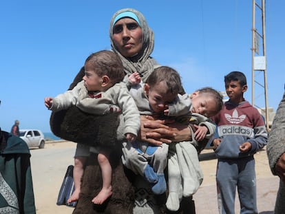 A Palestinian woman fleeing Al Shifa hospital following an Israeli raid, carries her triplet children as she moves southward, amid the ongoing conflict between Israel and Hamas, in the central Gaza Strip March 21, 2024