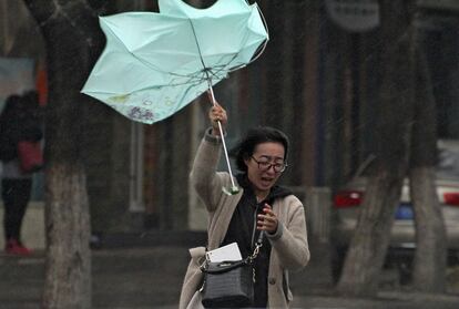 El fuerte viento dobla el paraguas de una mujer que camina bajo la lluvia en Yantai, China.