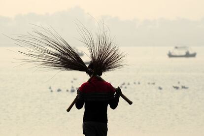 Un trabajador indio con un par de escobas ante el Sangam, la confluencia de los tres ríos Ganges, Yamuna y Saraswati. El festival Magh Mela se celebra todos los años en las orillas del Triveni Sangam durante el mes hindú de Magh.