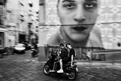 Dos amigos pasan en motocicleta ante el mural gigante con el rostro de Ugo Russo en la Piazzetta Parrocchiella, en una de las zonas calientes de Nápoles.