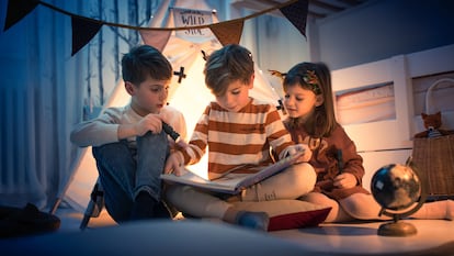 tres niños con una linterna mirando un libro y escondidos en su fuerte.