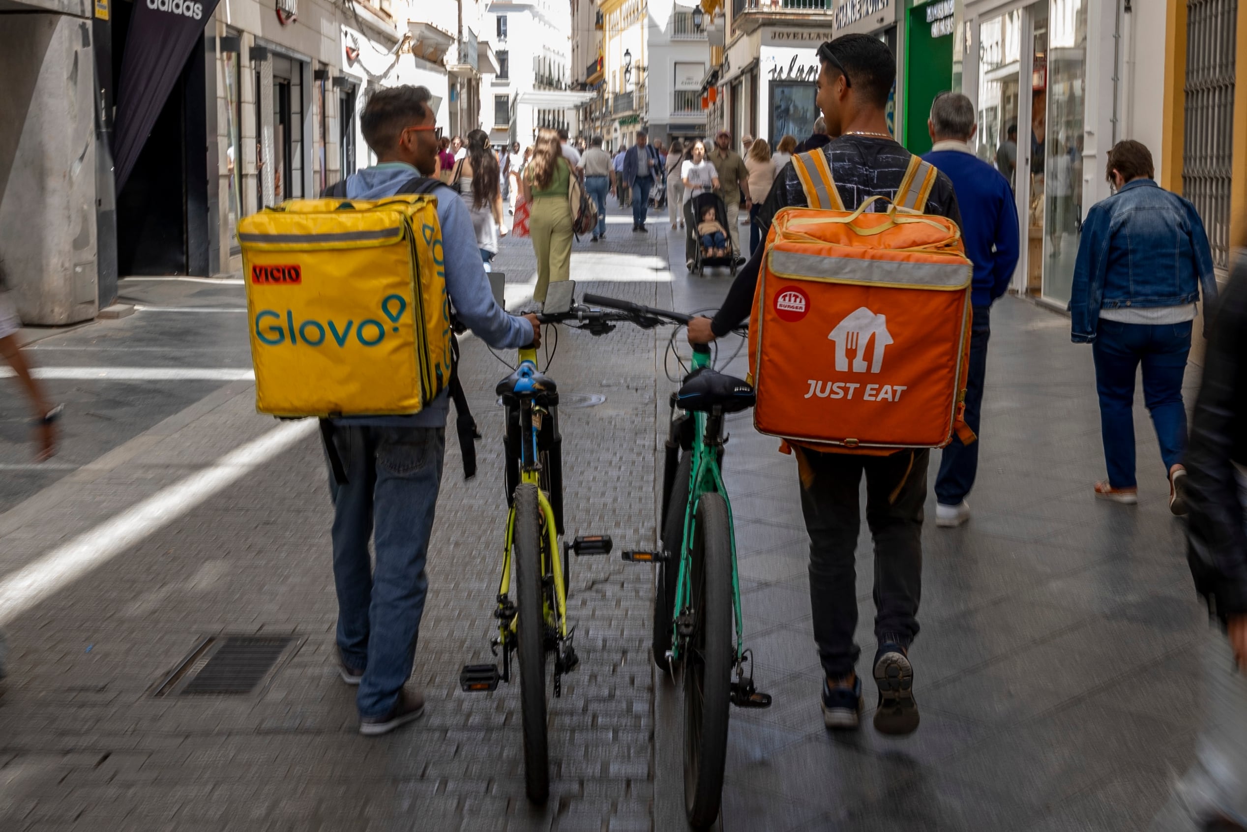 Repartidores con las mochilas de Just Eat y Glovo, en Sevilla en mayo de 2024. 