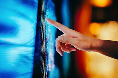 La mano de una mujer tocando una pantalla LED iluminada.