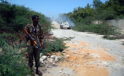 Un soldado gubernamental somalí vigila una carretera en el sur de Mogadiscio, mientras un carro de combate de la Misión de la Unión Africana en Somalia avanza sobre la pista de arena.