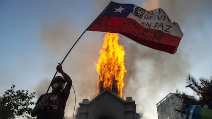 Manifestante balança bandeira chilena diante de igreja incendiada em Santiago, neste domingo.