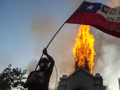 Manifestante balança bandeira chilena diante de igreja incendiada em Santiago, neste domingo.