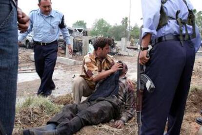 Un ciudadano socorre a uno de los heridos en la explosión de ayer en Bagdad, rodeado de agentes de la policía iraquí.
